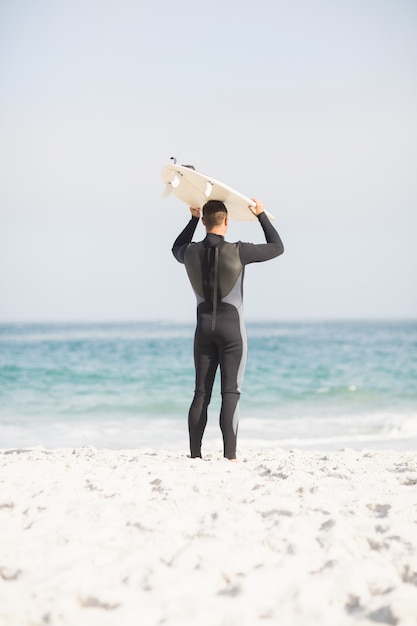 Vista trasera del hombre con tabla de surf sobre la cabeza