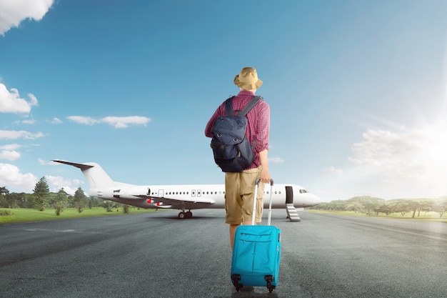 Vista trasera del hombre viajero asiático caminando con maleta al avión