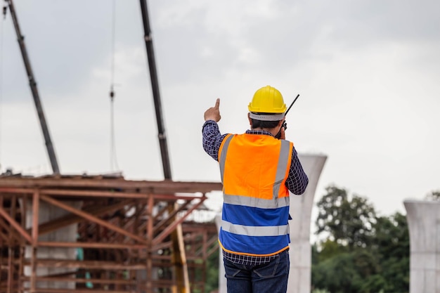 Foto vista trasera del ingeniero bajo proyecto de inspección y verificación en el sitio de construcción trabajador de capataz en casco en el sitio de construcción de infraestructura