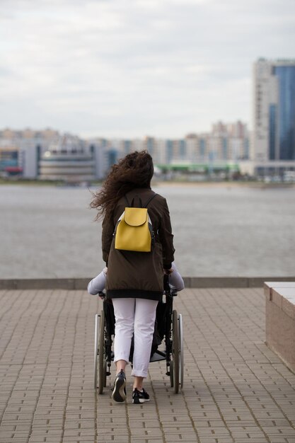 Vista trasera de una joven caminando con un discapacitado en silla de ruedas en el muelle