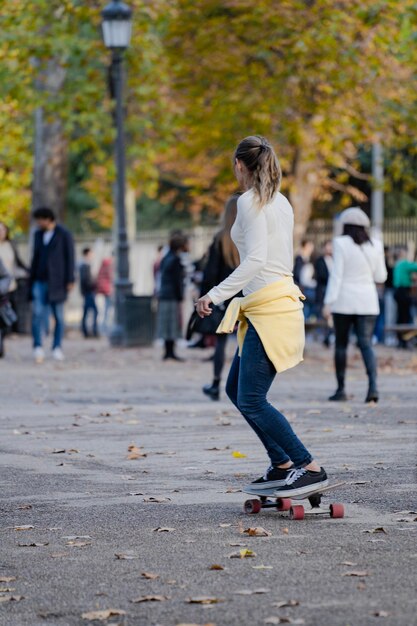 Vista trasera de una joven deportista montando en patineta en la carretera en un parque lleno de gente