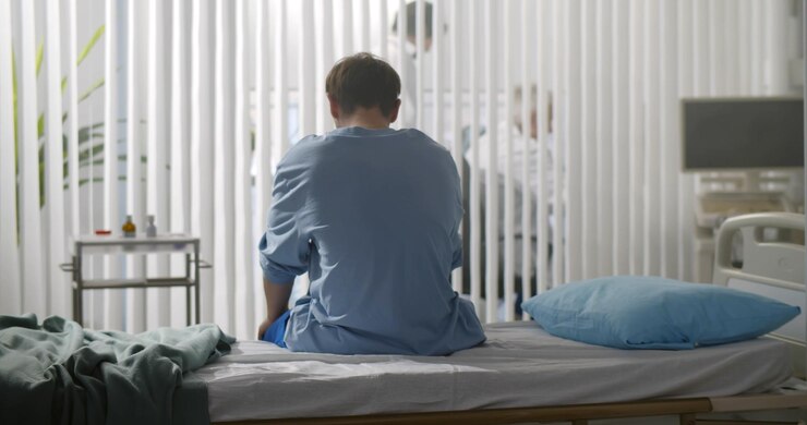 Vista trasera del joven desesperado sentado solo en la cama del hospital