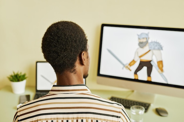 Vista trasera de un joven diseñador afroamericano dibujando una imagen gráfica de un guerrero mientras se sienta de frente
