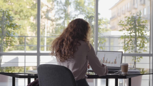 Vista trasera de una joven empresaria sentada en el escritorio y trabajando con documentos