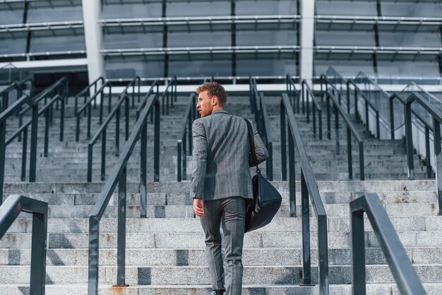 Vista trasera Joven empresario exitoso en ropa formal gris está al aire libre