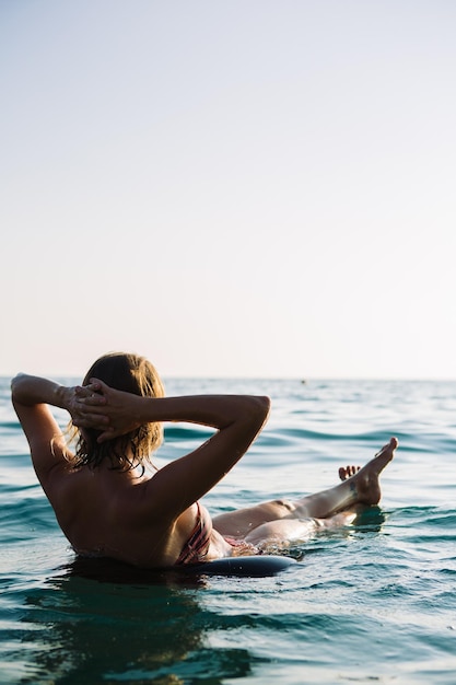 Vista trasera de una joven irreconocible con el pelo corto en bikini nadando en un anillo de aire con los brazos ensanchados y mirando hacia el paisaje marinoCopiar espacio