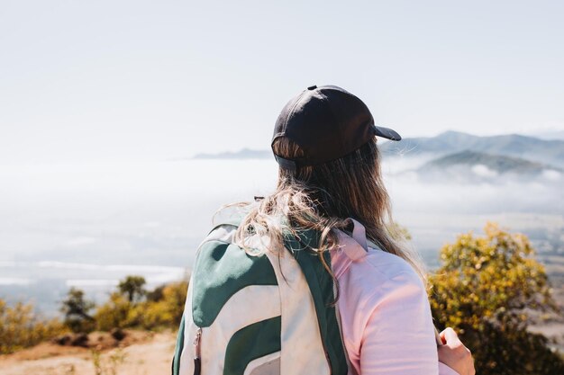 Vista trasera joven latina con mochila, contemplando la vista desde la cima de una colina