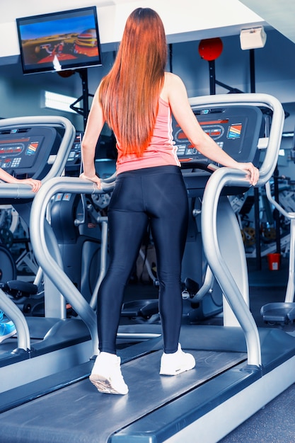 Foto vista trasera de la joven mujer en forma de ejercicio en una cinta en el gimnasio moderno y brillante