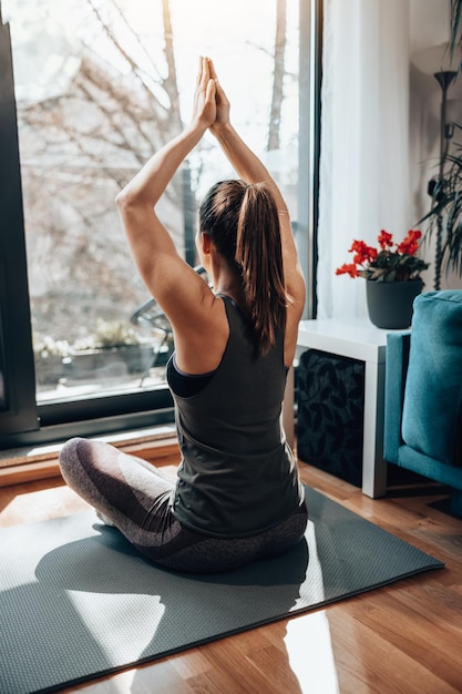 Vista trasera de una joven mujer linda meditando en la posición de yoga en casa por la mañana.