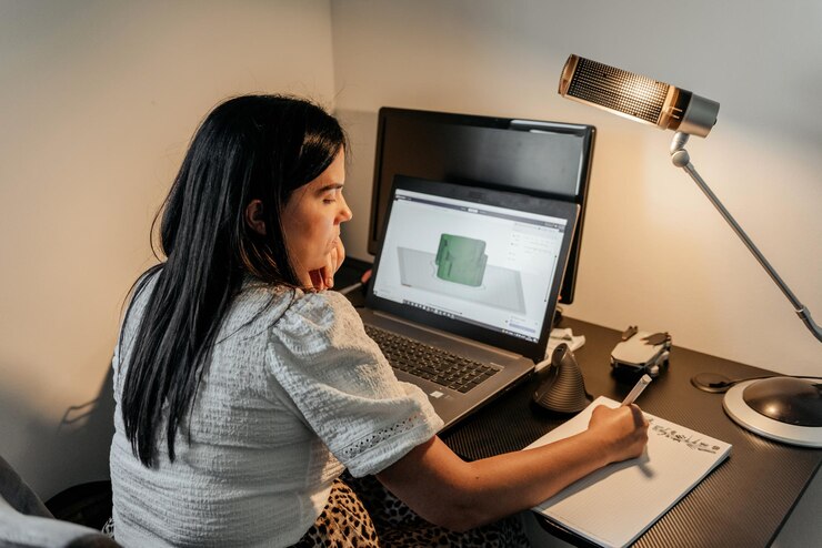 Foto vista trasera de una joven mujer de negocios sentada en un escritorio usando una computadora portátil y un software de diseño 3d