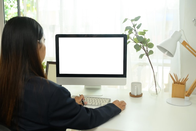 Vista trasera de una joven mujer de negocios trabajando en la computadora en una oficina doméstica brillante