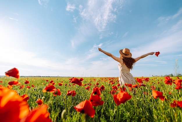 Vista trasera Joven mujer rizada con sombrero posando en el campo de amapolas Paisaje de verano