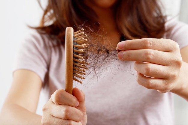 Vista trasera joven preocupada por el problema de pérdida de cabello, desequilibrio hormonal, concepto de estrés. Muchos cabellos caen después de peinarse con el cepillo en la mano. La mujer desenredó su cabello con un peine, Atención médica