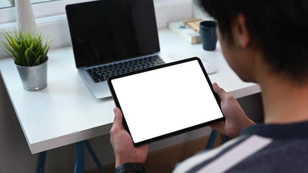 Foto vista trasera del joven sentado frente a la computadora portátil y con tableta digital en la oficina en casa.