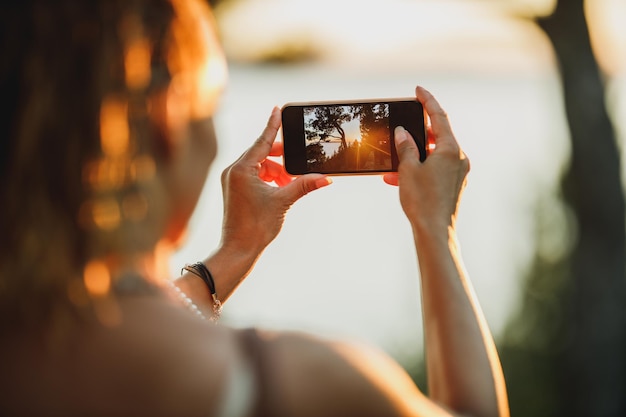 Foto vista trasera de una joven tomando fotos con su smartphone mientras disfruta de unas vacaciones de verano.