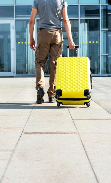 Foto vista trasera de un joven viajero con ropa informal que lleva una maleta amarilla junto a la entrada del aeropuerto fuera del concepto de turismo de viajes aéreos y vacaciones