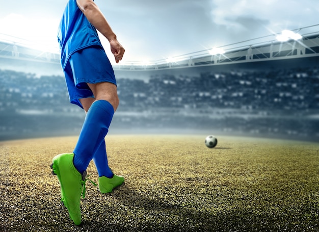 Vista trasera del jugador de fútbol asiático hombre pateando la pelota en el campo de fútbol