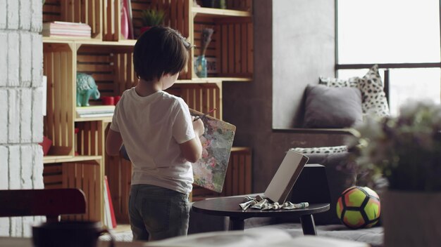 Vista trasera de un lindo niño caucásico pintando sobre lienzo en la sala de estar