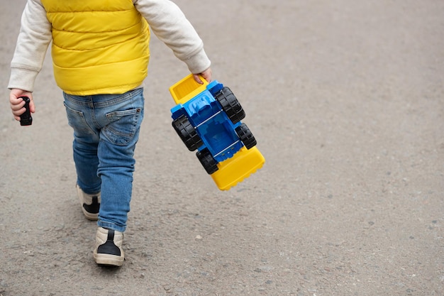 Vista trasera de un lindo niño corriendo por el camino en el parque con un gran tractor de plástico en la mano