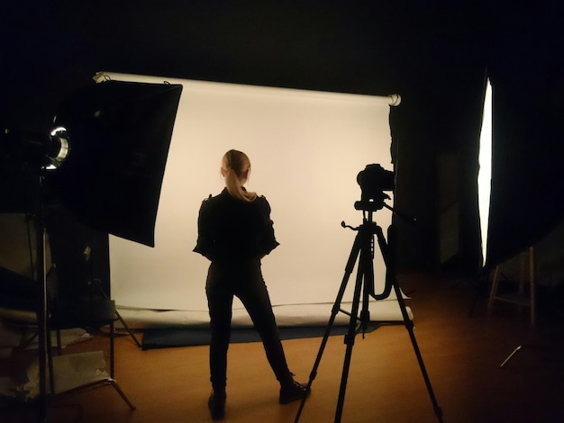 Vista trasera de longitud completa de una mujer de pie junto a un trípode en el estudio