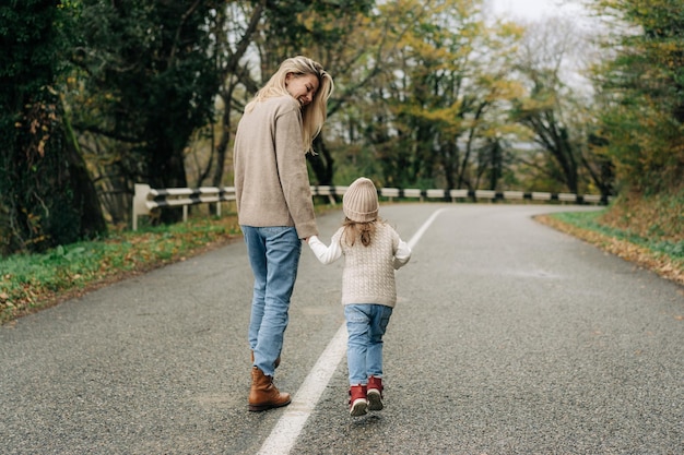 Foto vista trasera de una madre caminando por una carretera rural con su hija pequeña