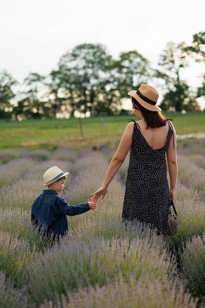 Vista trasera de madre e hijo caminando de la mano en el campo de lavanda