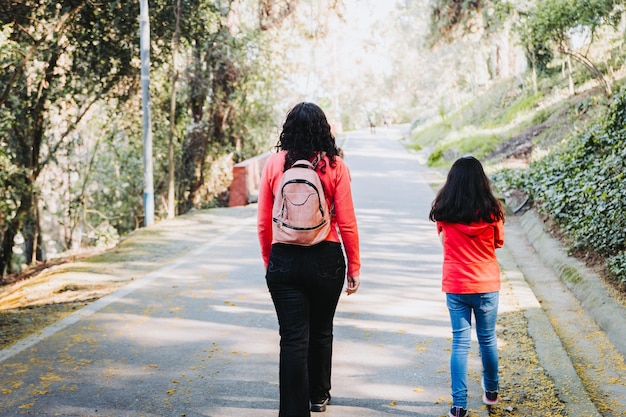 Vista trasera de una madre y su hija caminando por la carretera del parque