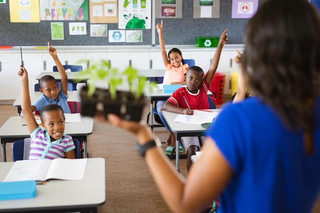 Vista trasera de una maestra sosteniendo plántulas de plantas mientras enseña en la clase en la escuela primaria