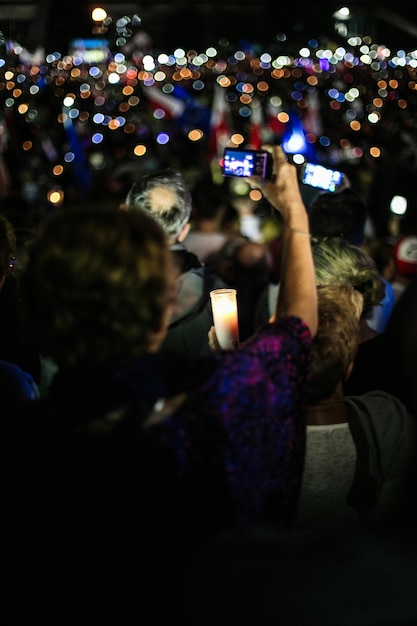 Vista trasera de una manifestante fotografiando con una cámara por la noche