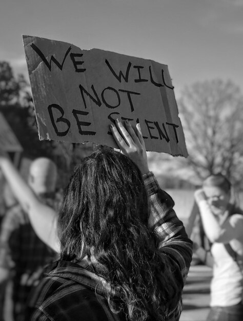 Foto vista trasera de una manifestante protestando con un cartel en la ciudad