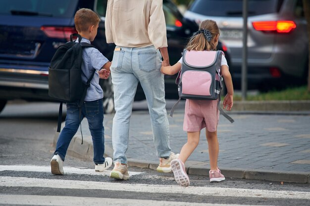 Foto vista trasera de la mano de la mujer con dos hijos van a la escuela concepción de la educación