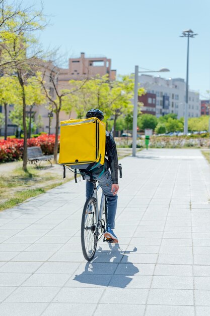 Una vista trasera del mensajero en bicicleta masculino entregando paquetes en la ciudad.