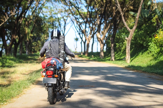 Vista trasera de un motociclista con chaqueta negra y casco montando una motocicleta a lo largo de una carretera de campo entre tal