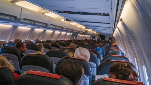 La vista trasera de las muchas personas en el avión Interior del avión con pasajeros sentados en los asientos El concepto de viajar