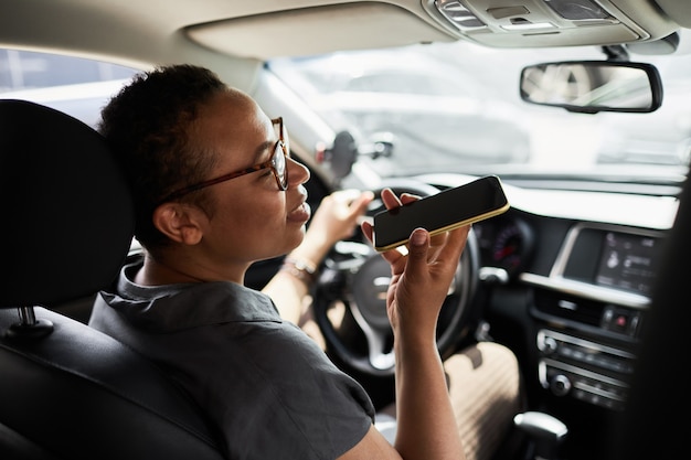 Vista trasera de la mujer africana en anteojos hablando por teléfono móvil durante su conducción