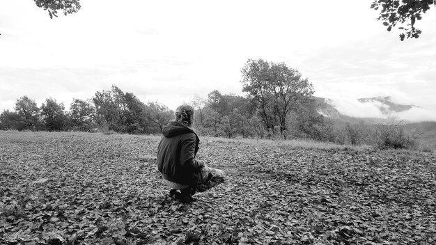 Vista trasera de una mujer agachada en el campo contra el cielo