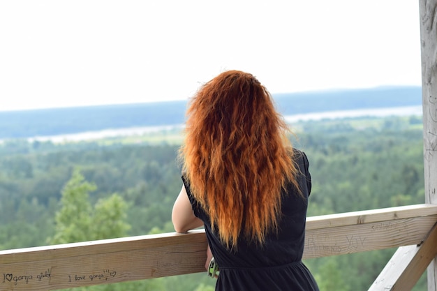 Foto vista trasera de una mujer apoyada en una barandilla contra un paisaje verde