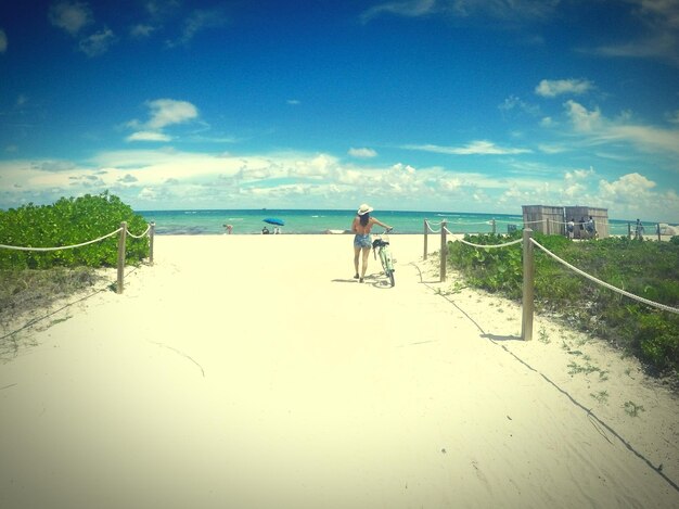 Foto vista trasera de una mujer con bicicleta en la playa