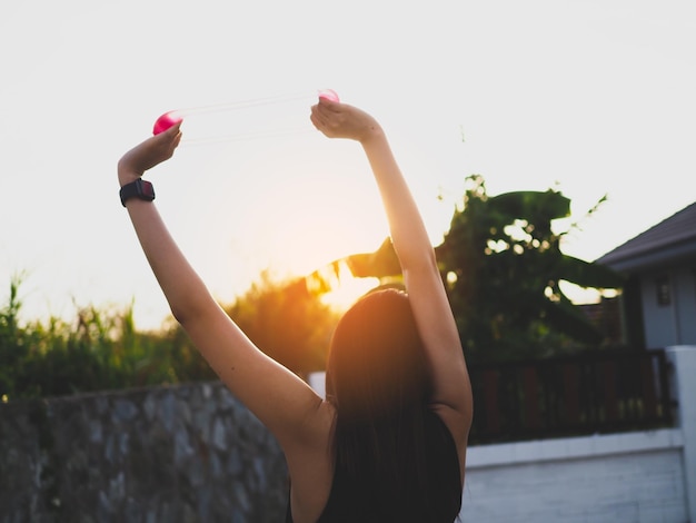 Foto vista trasera de una mujer con los brazos levantados estirándose contra el cielo durante la puesta de sol