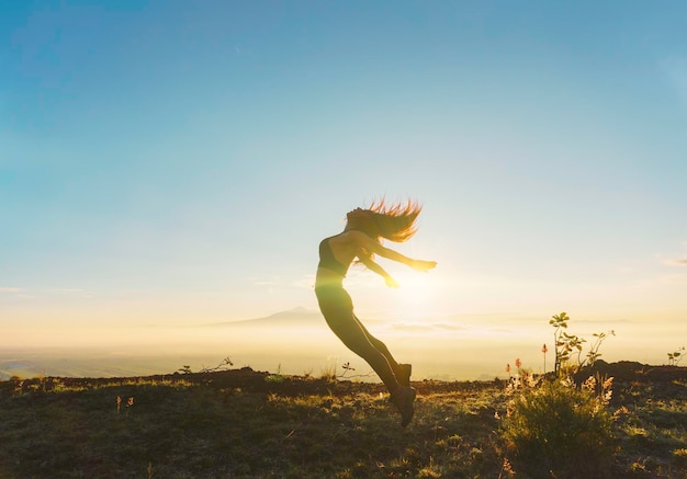 Vista trasera de una mujer con los brazos levantados de pie contra el cielo durante la puesta de sol