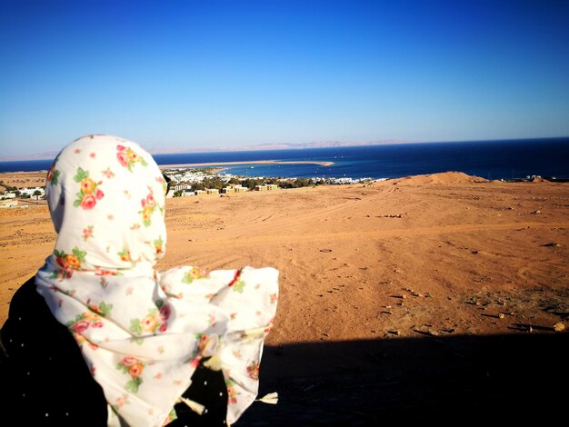 Foto vista trasera de una mujer con una bufanda mientras está de pie en la playa contra el cielo