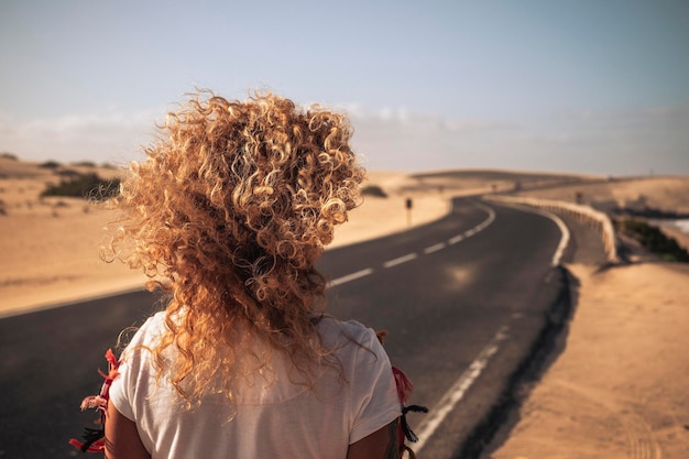 Foto vista trasera de una mujer con el cabello rizado de pie en la carretera contra el cielo