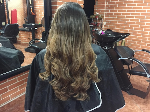 Foto vista trasera de una mujer con cabello rubio mientras está sentada en una silla en una peluquería