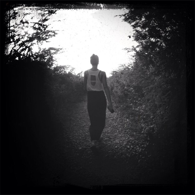 Foto vista trasera de una mujer caminando por un camino de tierra en el bosque