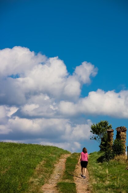 Vista trasera de una mujer caminando por el campo contra un cielo nublado