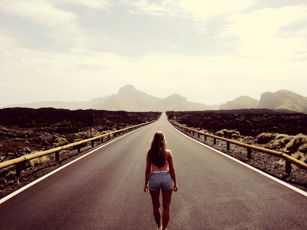 Foto vista trasera de una mujer caminando por la carretera contra el cielo