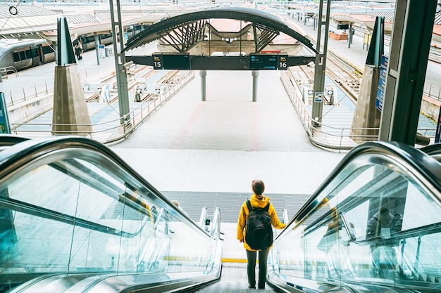 Vista trasera de una mujer caminando por la escalera mecánica en un centro comercial