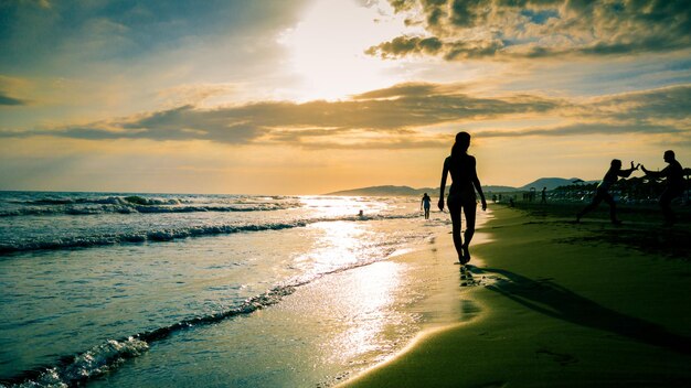 Vista trasera de una mujer caminando por la playa al atardecer
