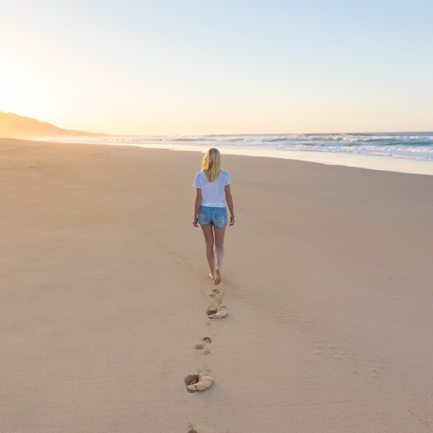 Foto vista trasera de una mujer caminando por la playa contra el cielo