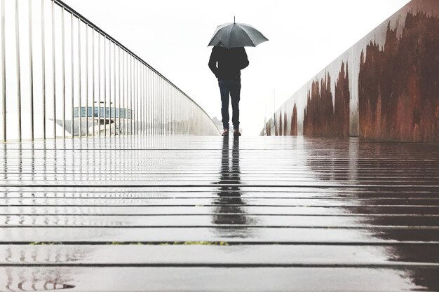 Vista trasera de una mujer caminando sobre un paraguas mojado durante la temporada de lluvias